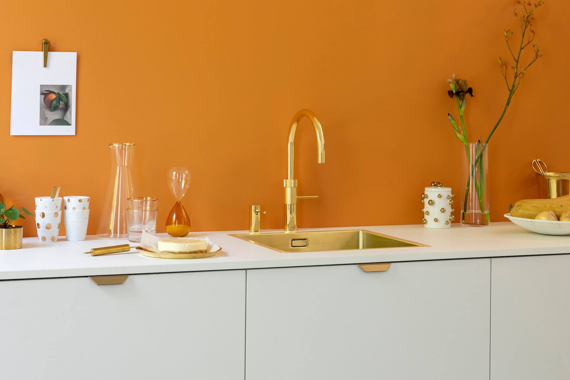 Goldfarbener Quooker Wasserhahn vor orangefarbener Wand